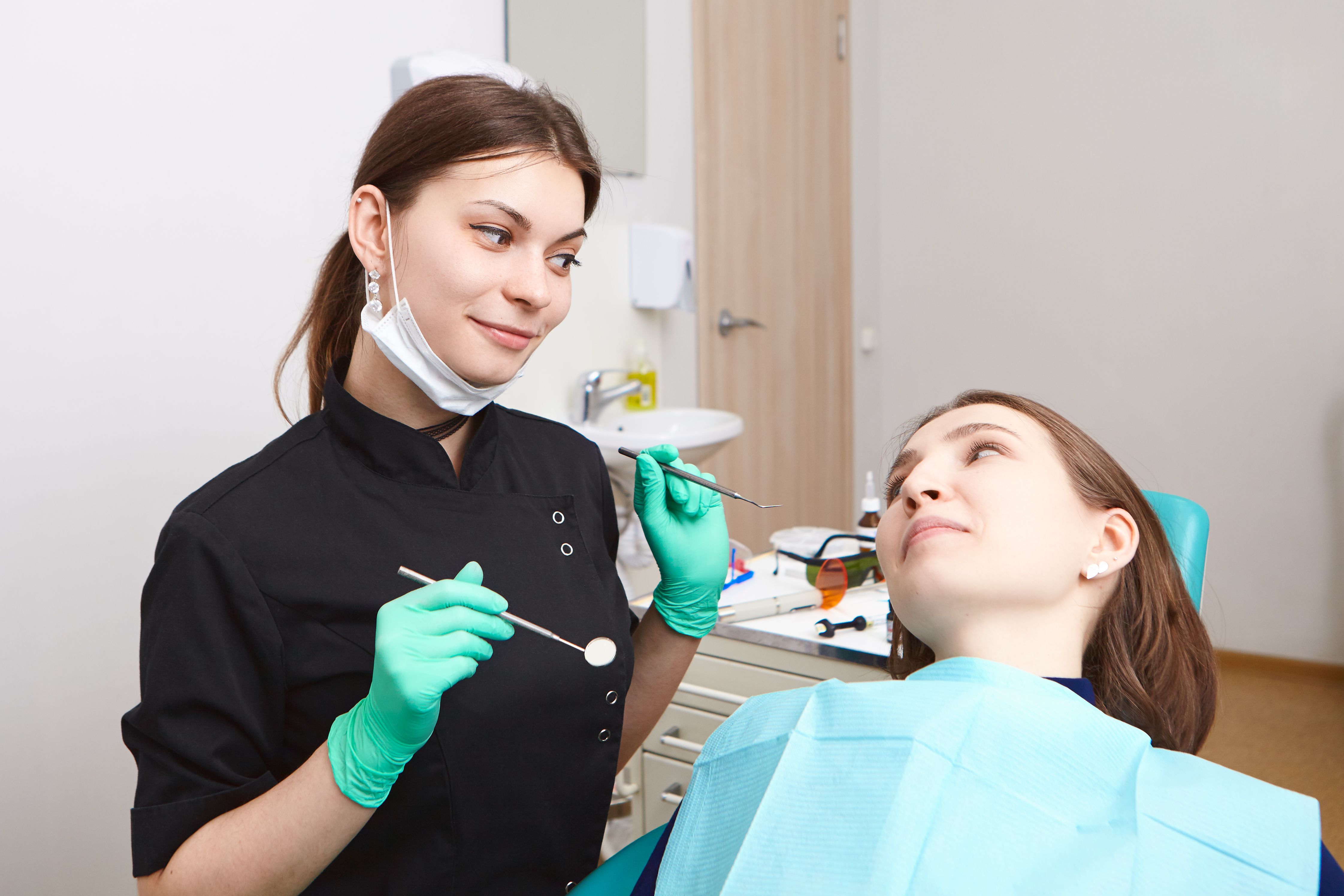 experienced-attractive-young-brunette-woman-dentist-holding-dental-tools-while-checking-teeth-female-patient-cavities