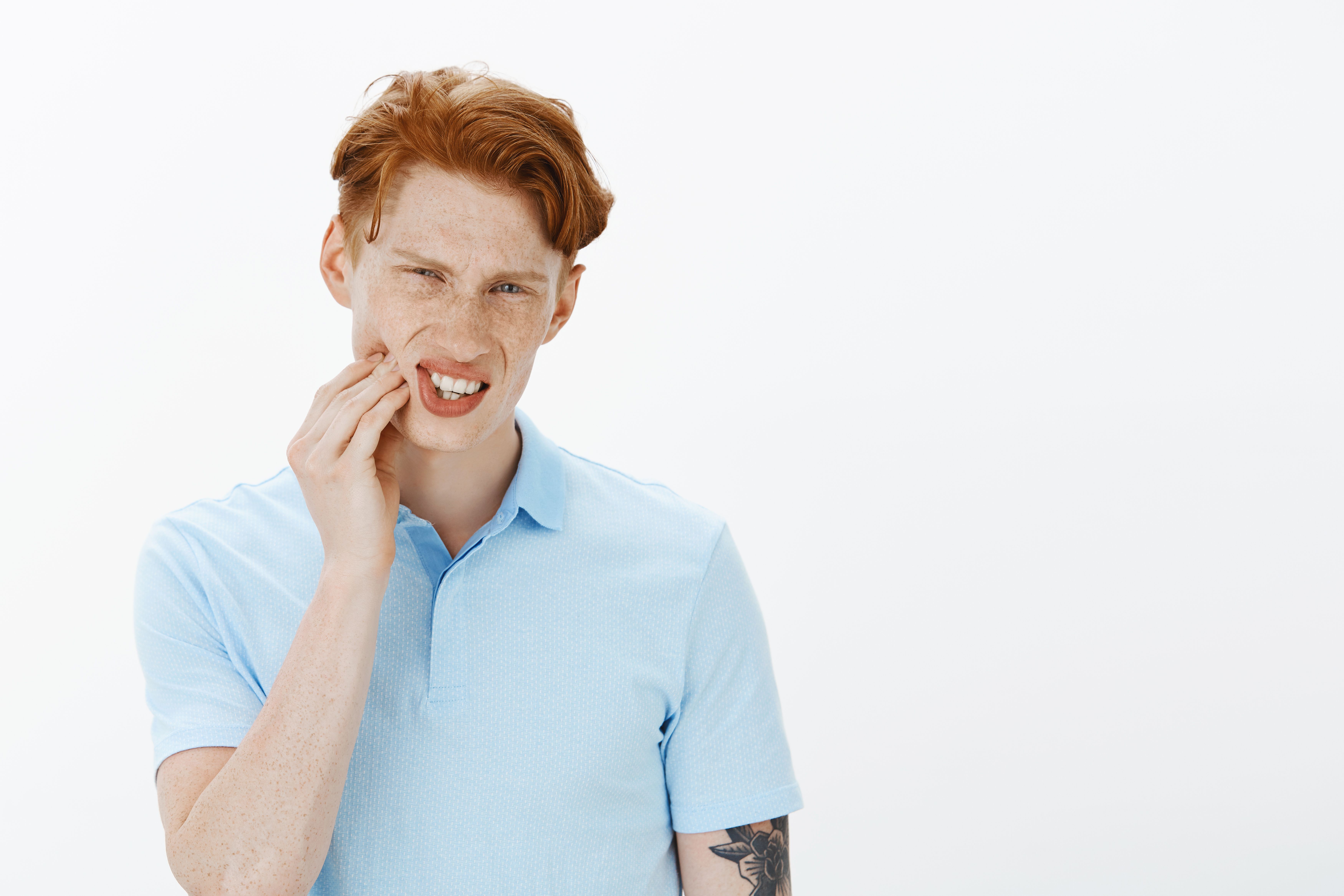 grimacing-redhead-man-complaining-toothache-touching-cheek-feeling-pain