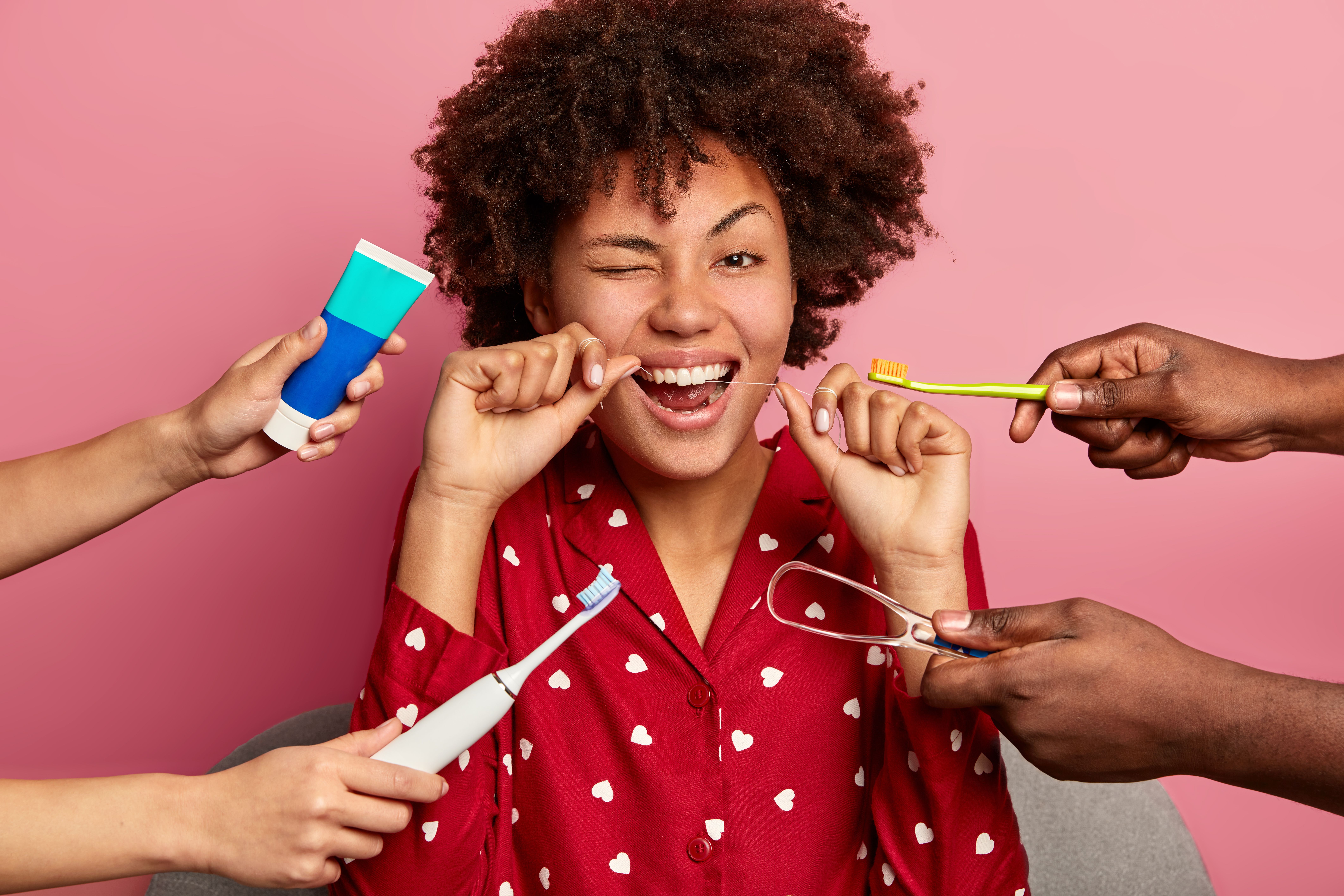 happy-curly-young-woman-brushes-teeth-with-tooth-floss-cares-about-oral-hygiene-surrounded-with-toothpaste-electric-toothbrush-tongue-cleaner.jpg